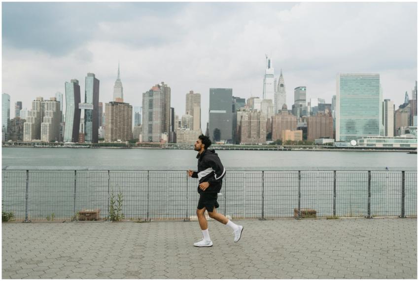 A man jogs along a riverside promenade with a city