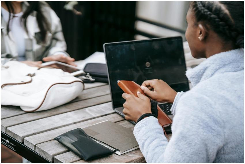 Two young women working together on a laptop outdo