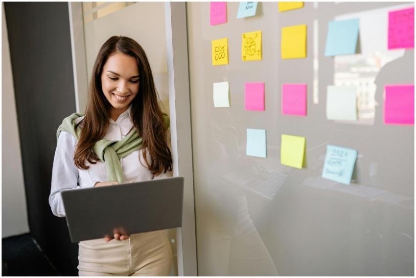Smiling woman uses laptop in office, planning with