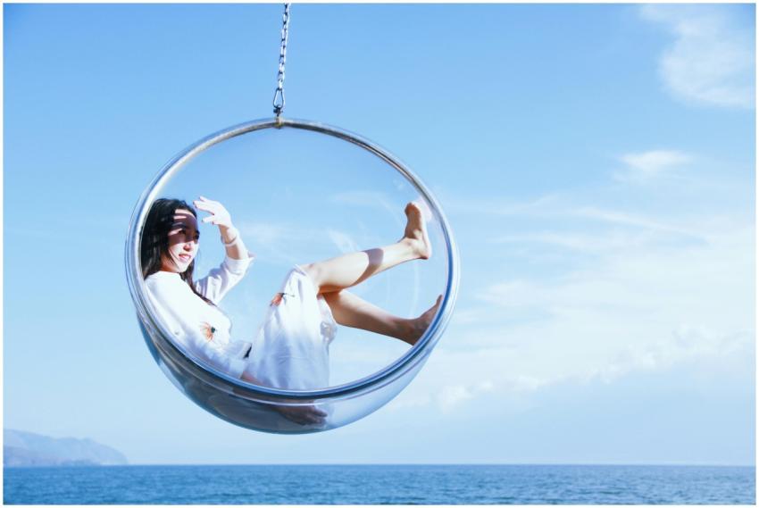 A woman enjoys a sunny day in a hanging bubble cha