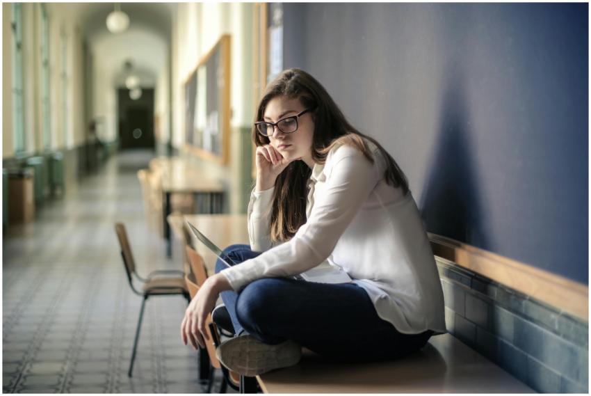 Thoughtful woman sitting alone in a school hallway