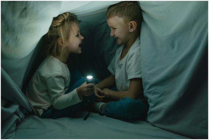 Two children giggle in a cozy blanket fort, sharin