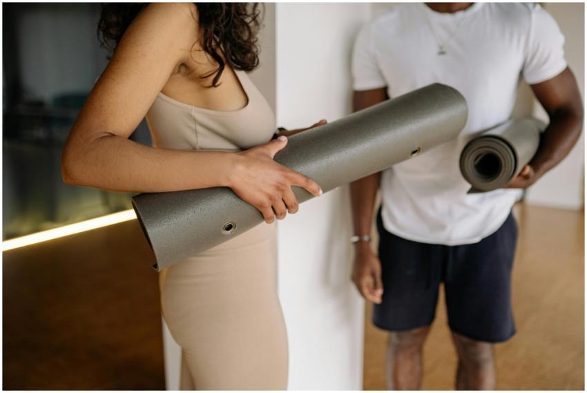 Two adults holding yoga mats in a studio, promotin