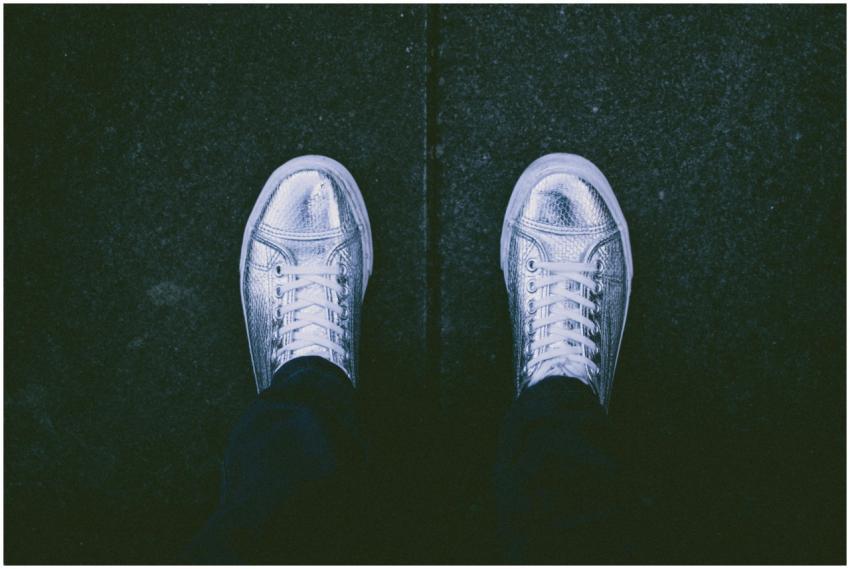 A top view of silver sneakers on a dark pavement b