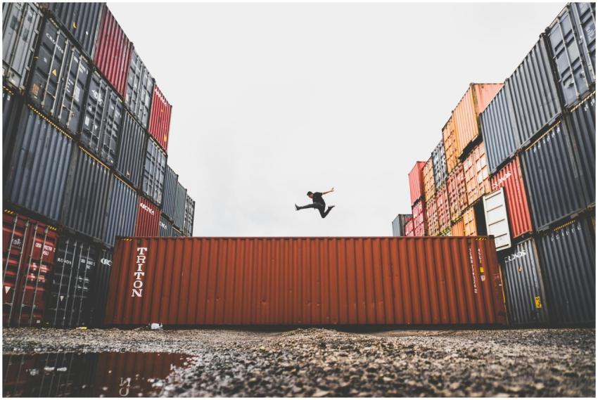 A person leaps dramatically above stacked shipping
