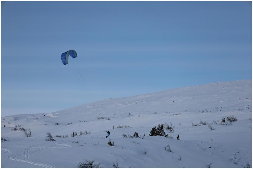 A person kiting over snow-covered mountains under