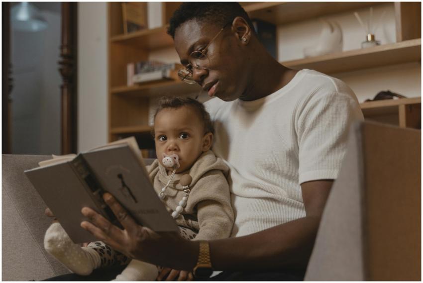 A father reads a book to his baby while sitting on