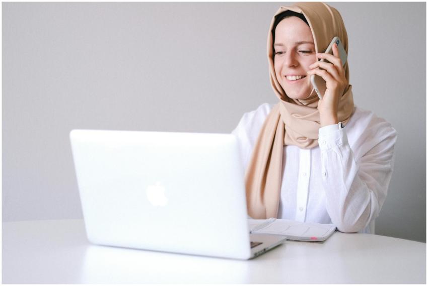 Smiling woman in a hijab uses laptop and phone at