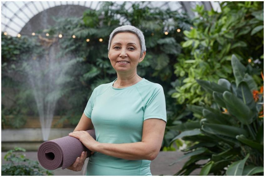 Elderly woman holding yoga mat and smiling in a lu