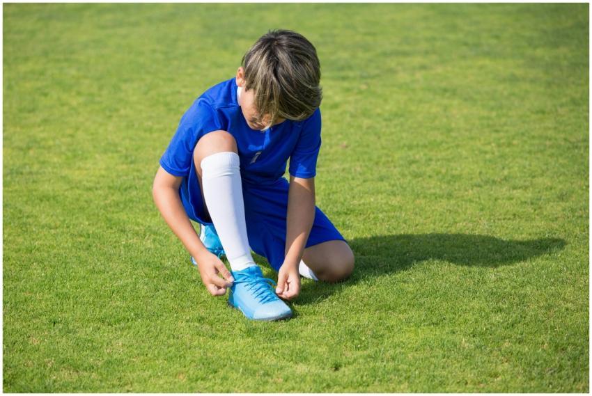 A child in a blue soccer uniform tying shoelaces o