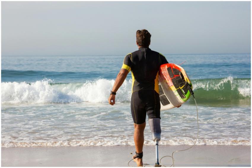 An inspiring image of an amputee surfer walking to