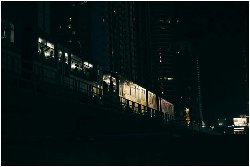 A train passes through a cityscape at night, illum