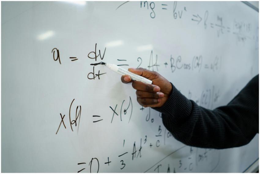 Close-up of hand writing equations on a whiteboard