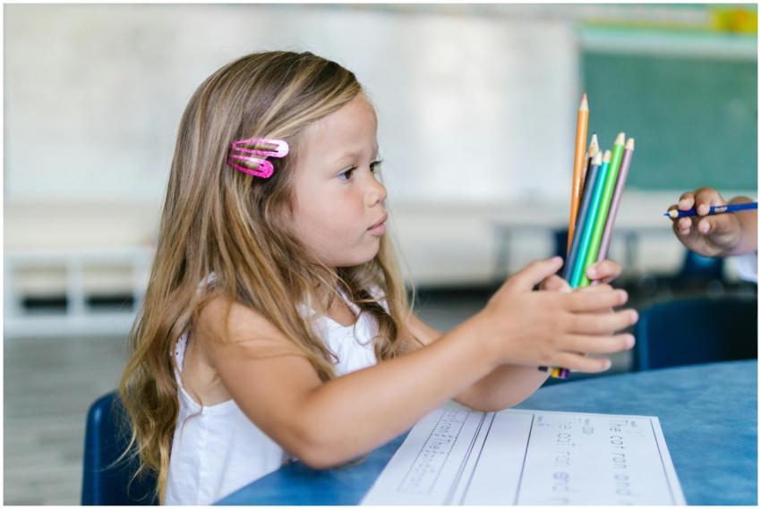 A young girl holds colored pencils while sitting a