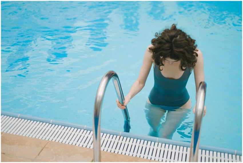 Young woman in a teal swimsuit using ladder to ent
