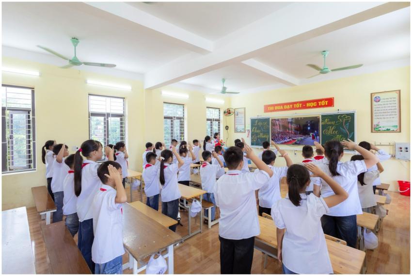 Students in uniforms saluting in a bright classroo