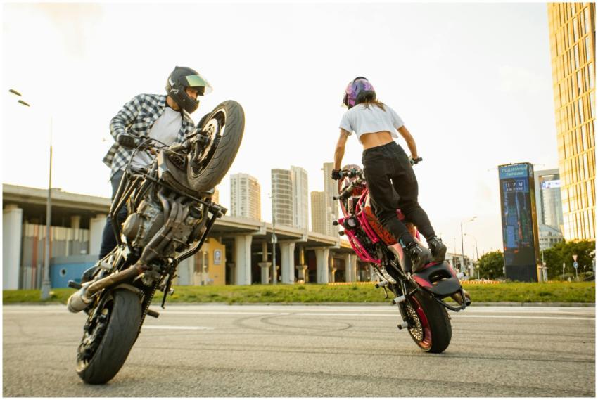 Two riders performing motorcycle stunts in a citys