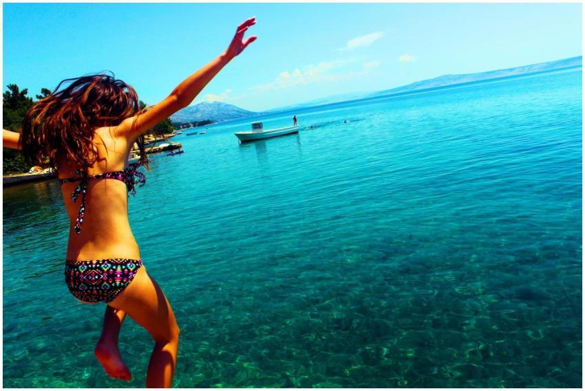 Young woman in a bikini jumps into crystal clear C