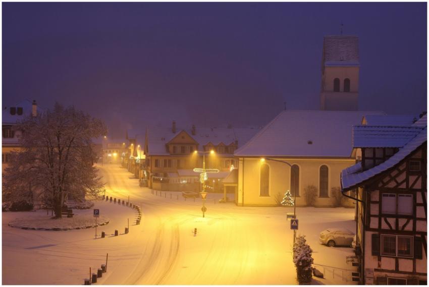 Quiet snowy village street with lights and church