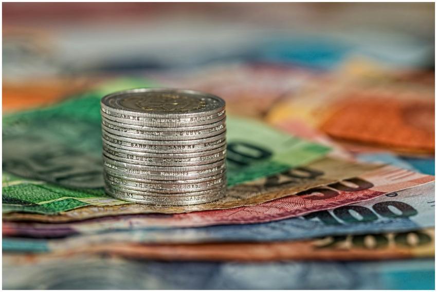 A stack of coins on top of various colored banknot