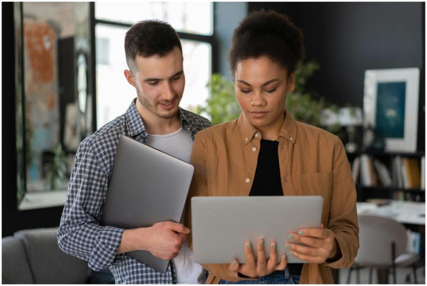 Two young adults collaborating with laptops in a s