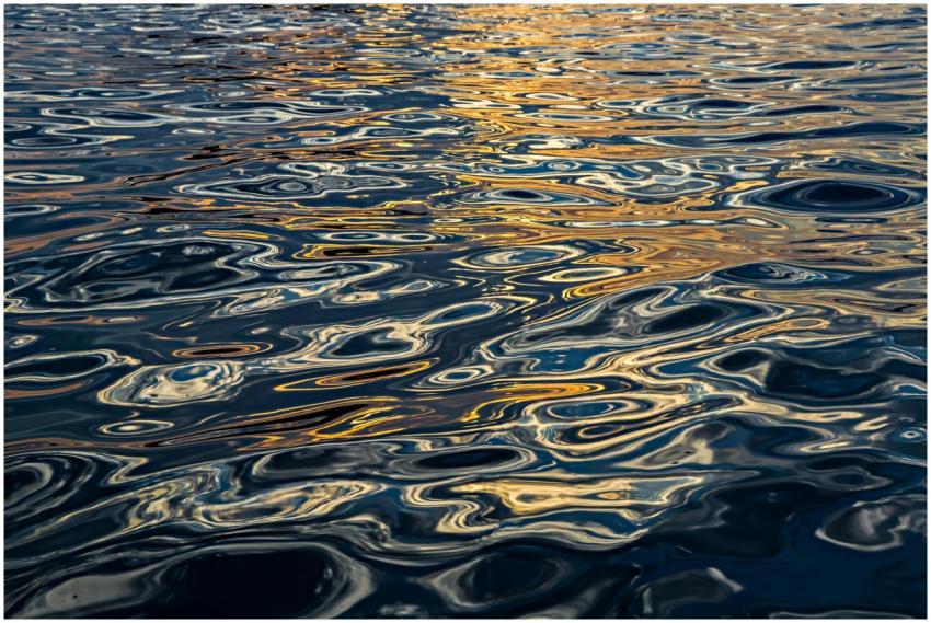 Rippling water surface reflecting sunset colors, c