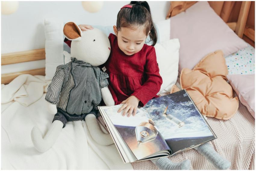 Child reading a picture book with a stuffed toy in