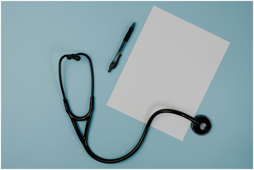Flat lay of stethoscope, blank paper, and pen on b