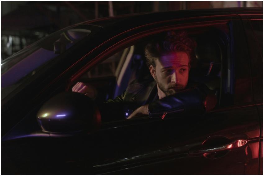 Bearded man in a car at night with moody lighting.