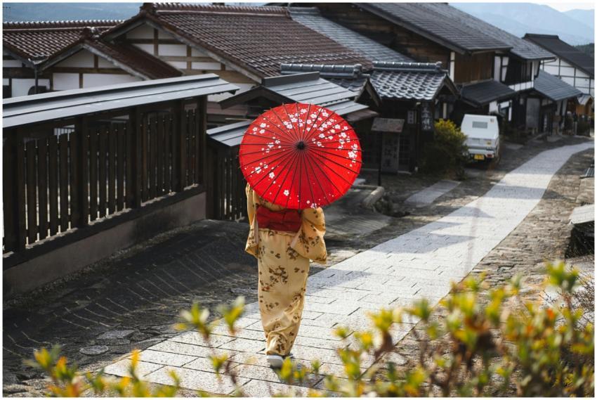Woman in kimono with red umbrella walking through