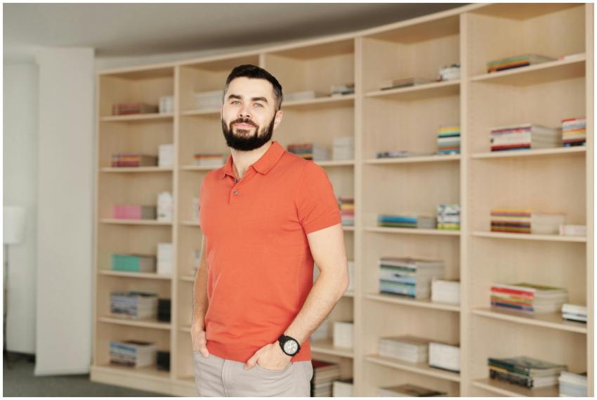 A young man with a beard stands confidently in a m