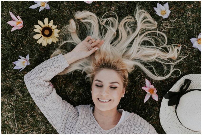 A smiling woman with closed eyes lies on grass, su