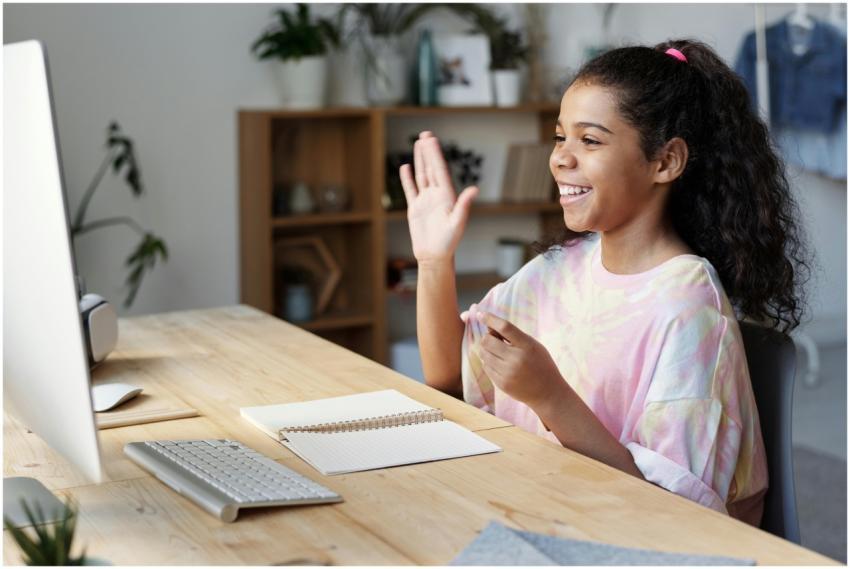 A happy girl waves during an online class at home,