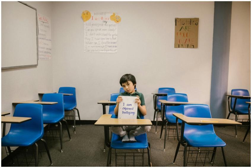 A child sits in an empty classroom, holding a sign