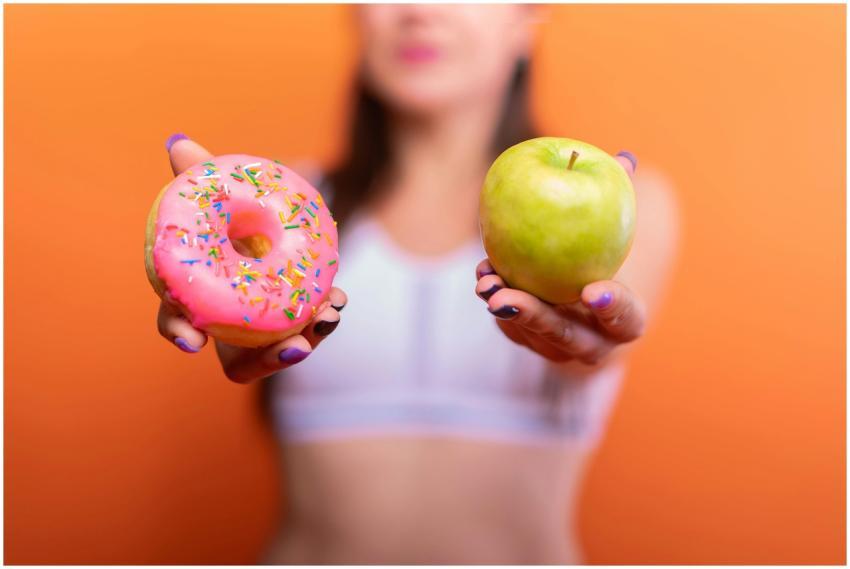 A woman holds a green apple and a pink donut with