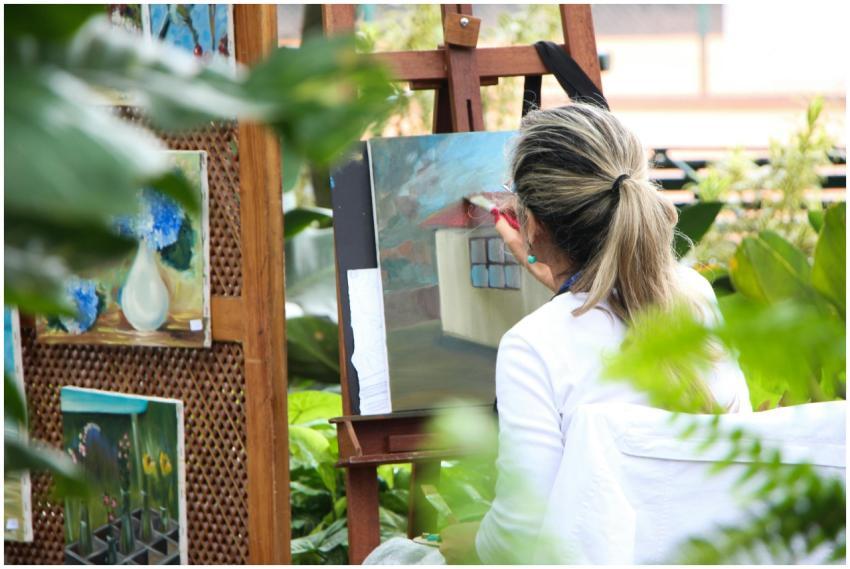 A woman enjoys painting in a lush outdoor garden,