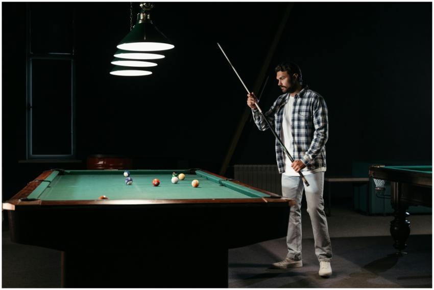 A man holding a cue stick prepares to play billiar