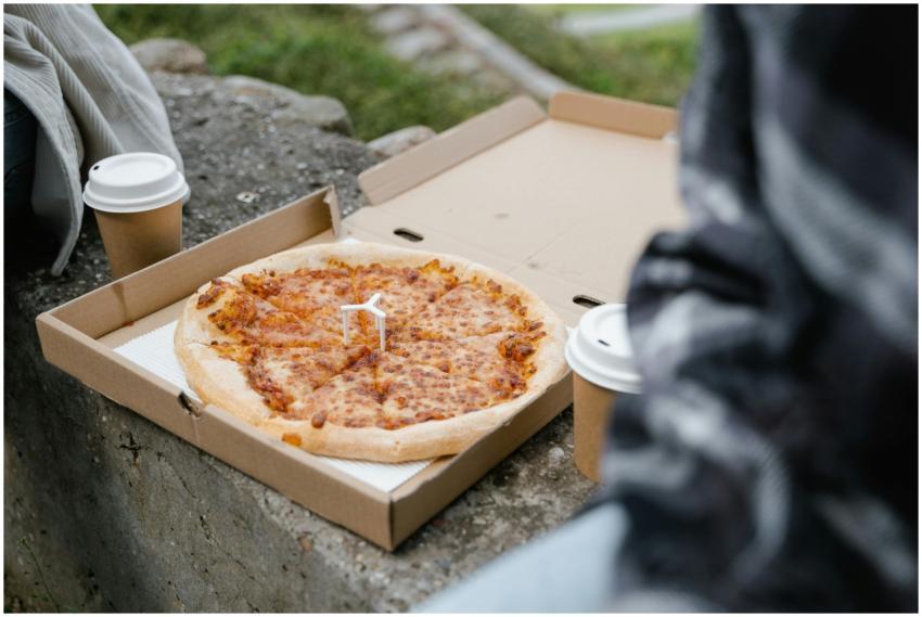 Close-up of a pizza in a box with coffee cups on a