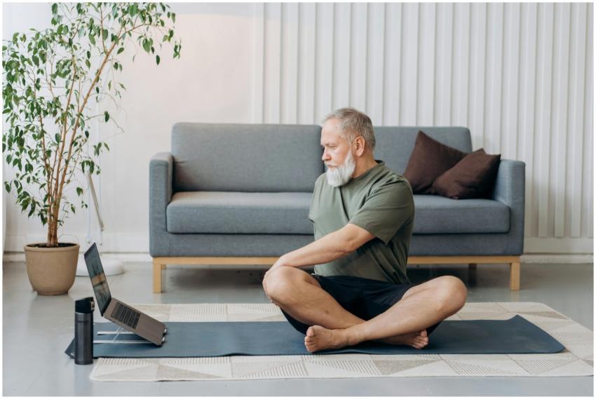 Senior man doing yoga on a mat at home, facing a l