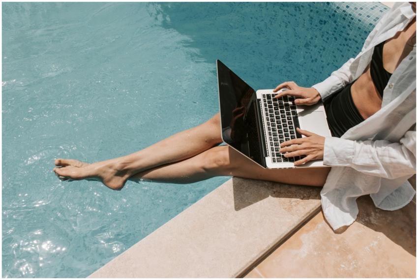 A woman in swimwear working on a laptop by the poo