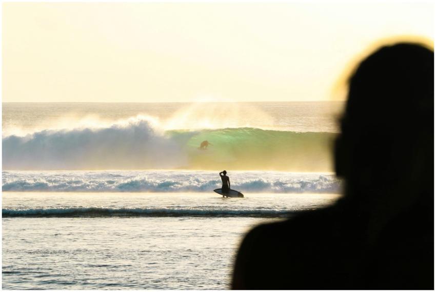 A silhouette of a surfer riding waves during sunse