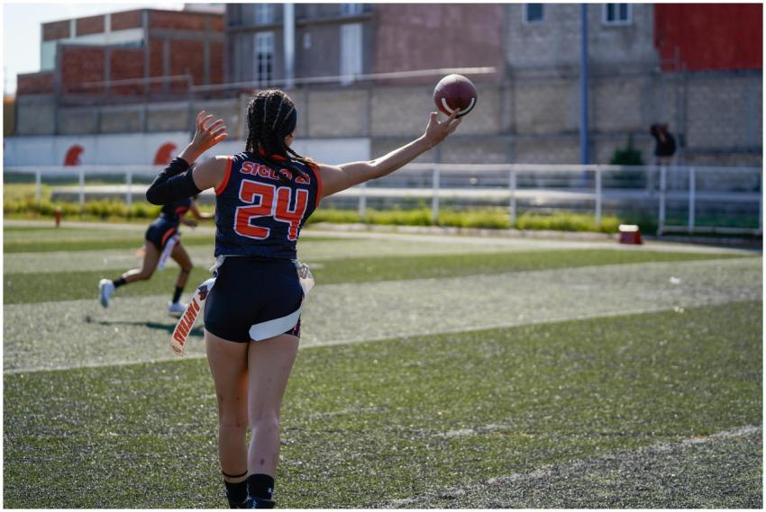 Two female athletes playing flag football on grass