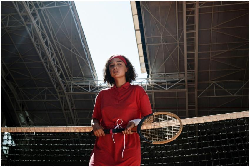 A woman in a red outfit stands with a tennis racke