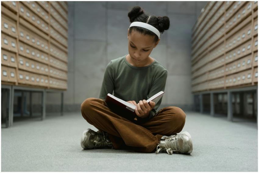 A young girl sitting cross-legged, reading a book