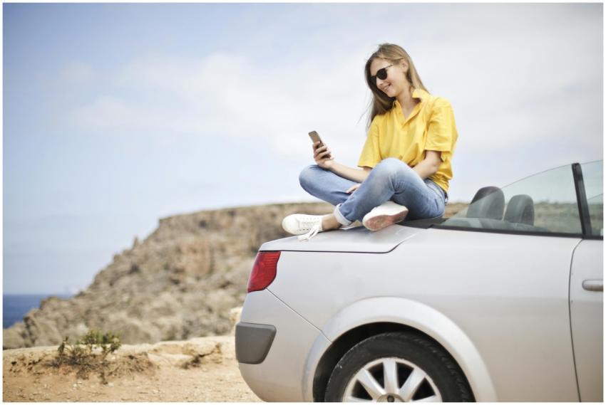Smiling young woman sitting on a car at the beach