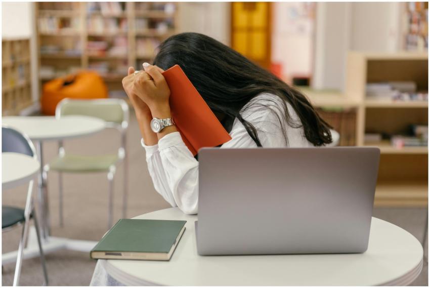 A student hides her face in a book, sitting at a l