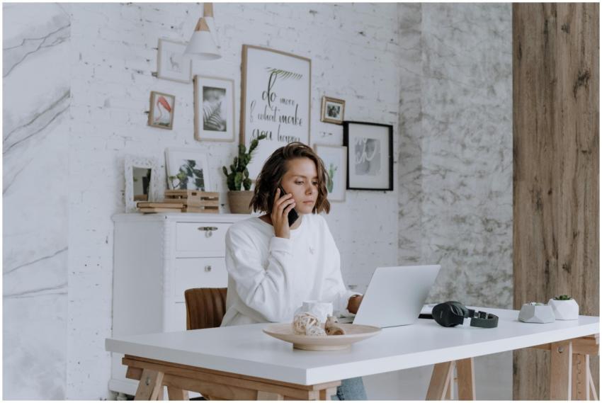 Woman talking on phone while using laptop in brigh
