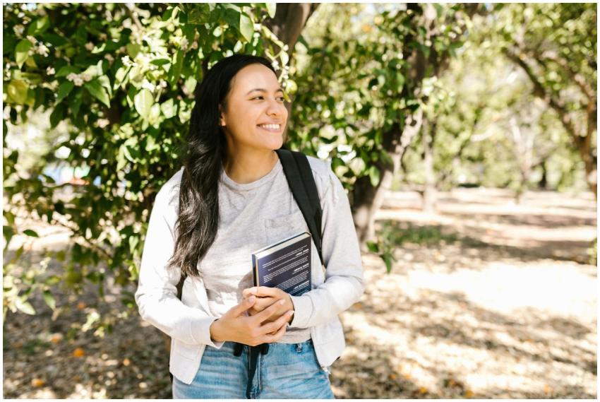 A young student with long hair holding a book, smi