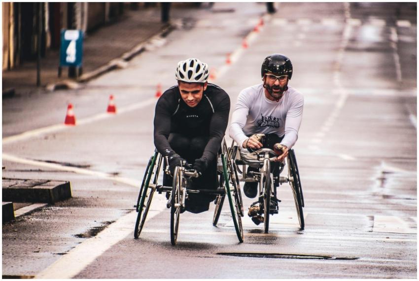 Two men compete in a wheelchair race on a wet urba