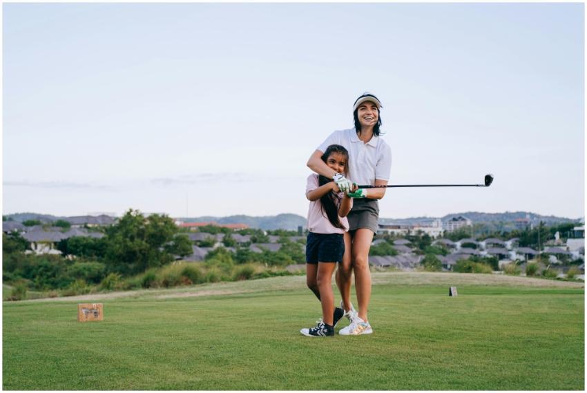 A mother teaches her daughter how to play golf on